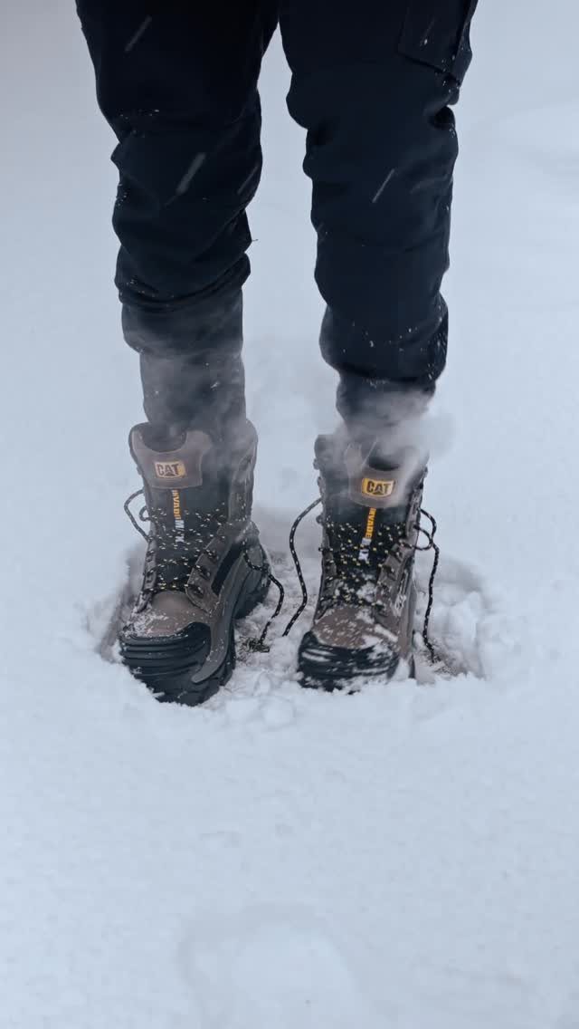 Brown CAT winter boots worn by a person standing in deep white snow