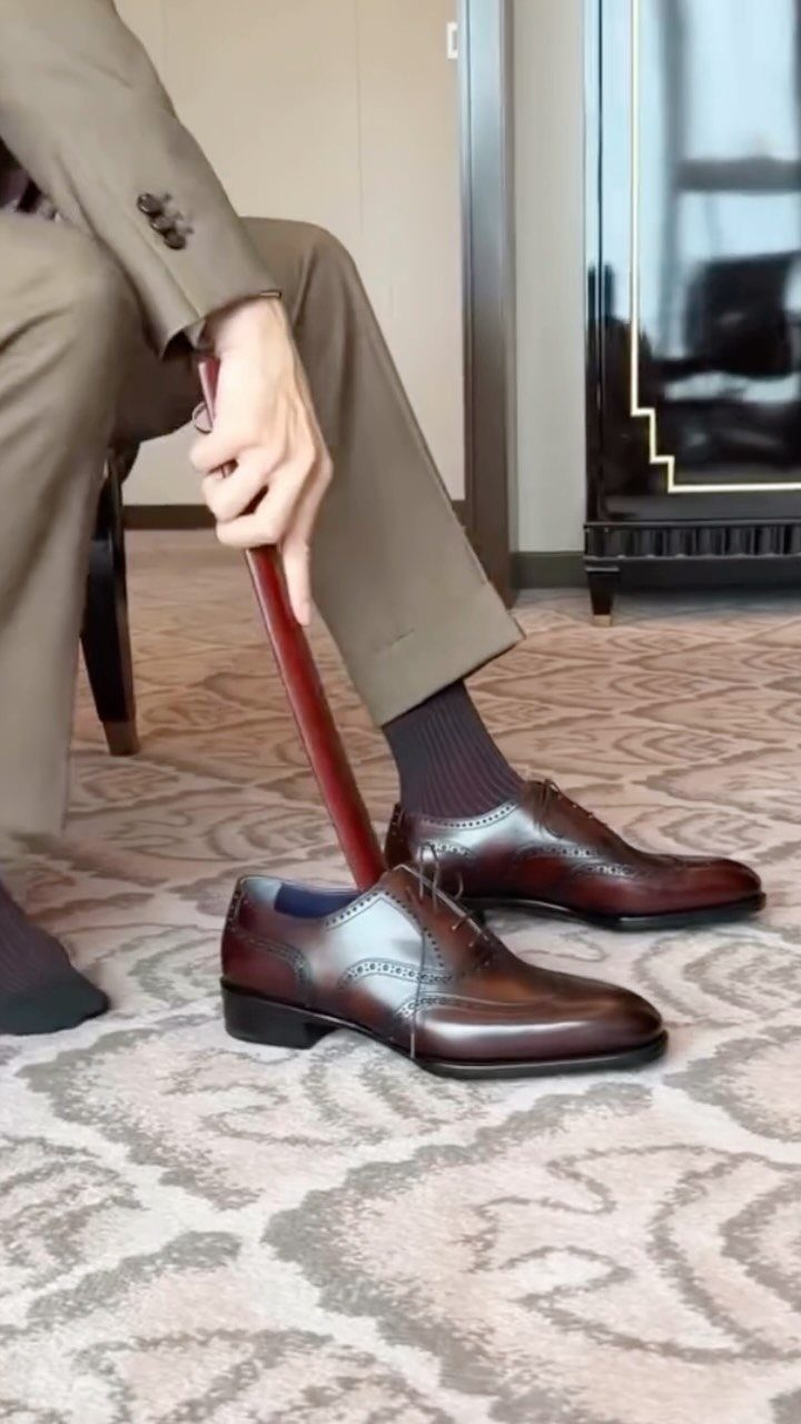 Brown leather lace-up oxford shoes being put on with a red shoehorn.