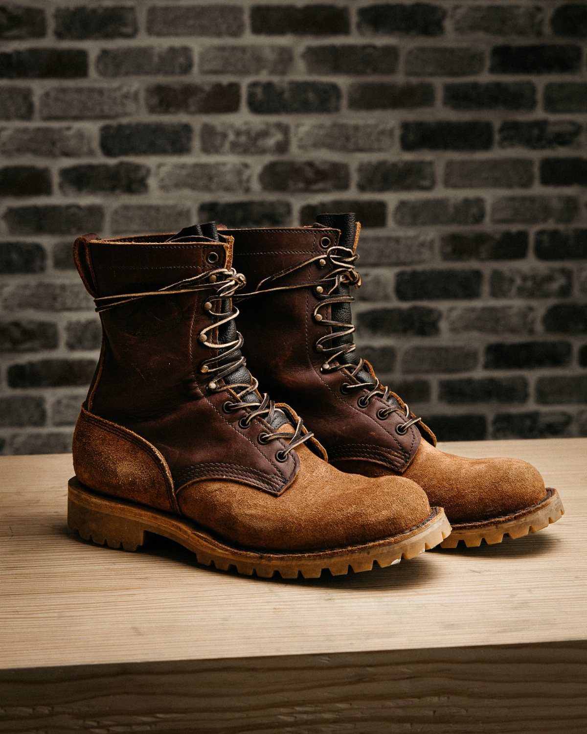 Brown leather work boots with thick soles on a wooden surface against brick.