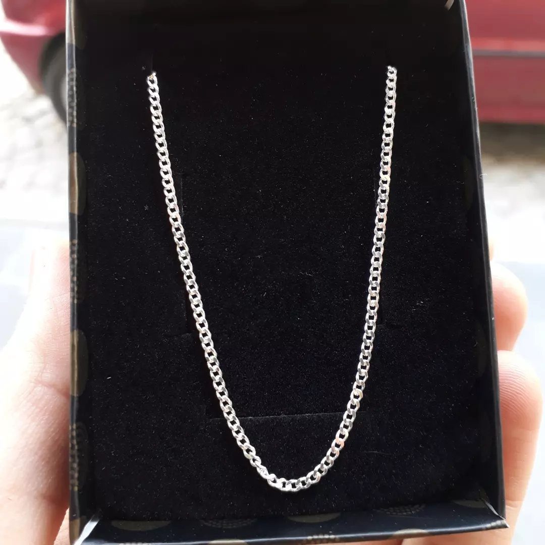 Silver metal chain resting in a black velvet jewelry box held by hand
