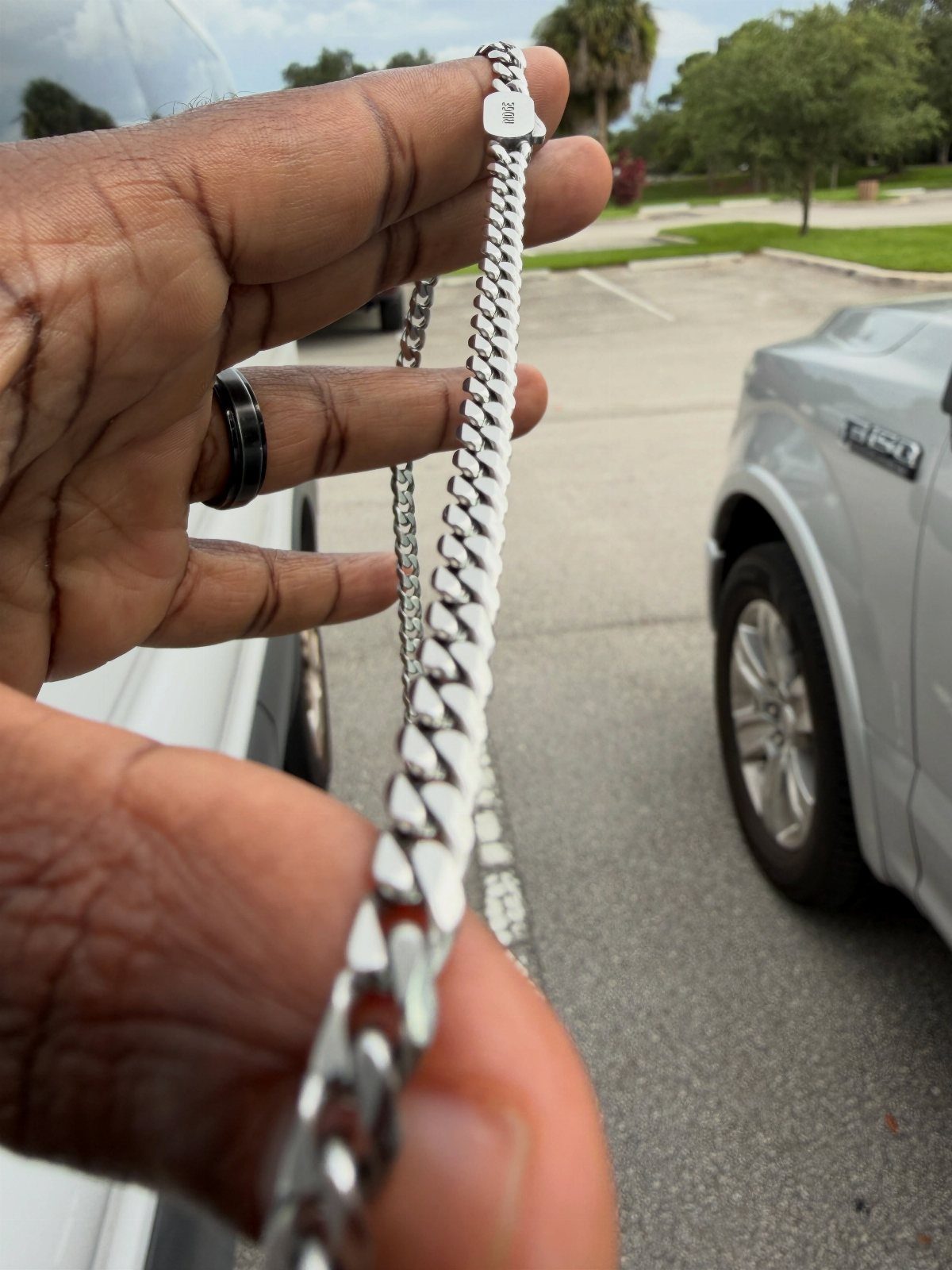 Silver curb chain necklace held by a hand in an outdoor parking lot