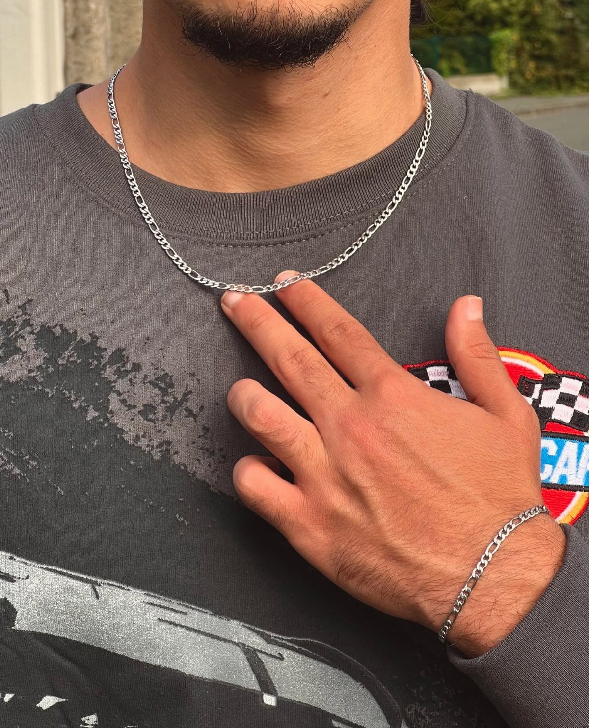 Silver Figaro chain necklace and bracelet worn by a man in grey shirt