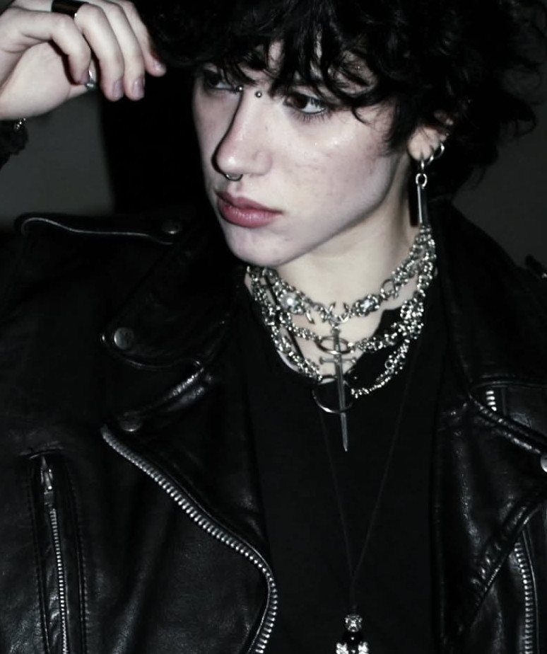Person in leather jacket wearing multiple layered silver chains with a sword pendant