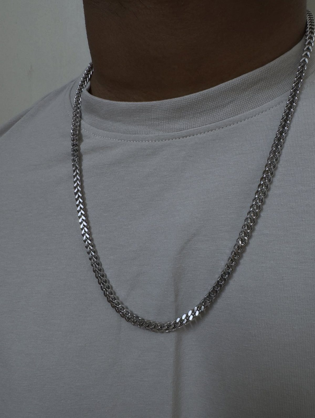 Silver metal chain necklace with a dense woven link worn over grey shirt