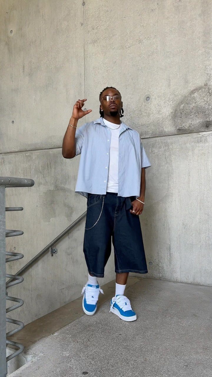 Man in blue button-down shirt and wide shorts wearing blue and white sneakers.