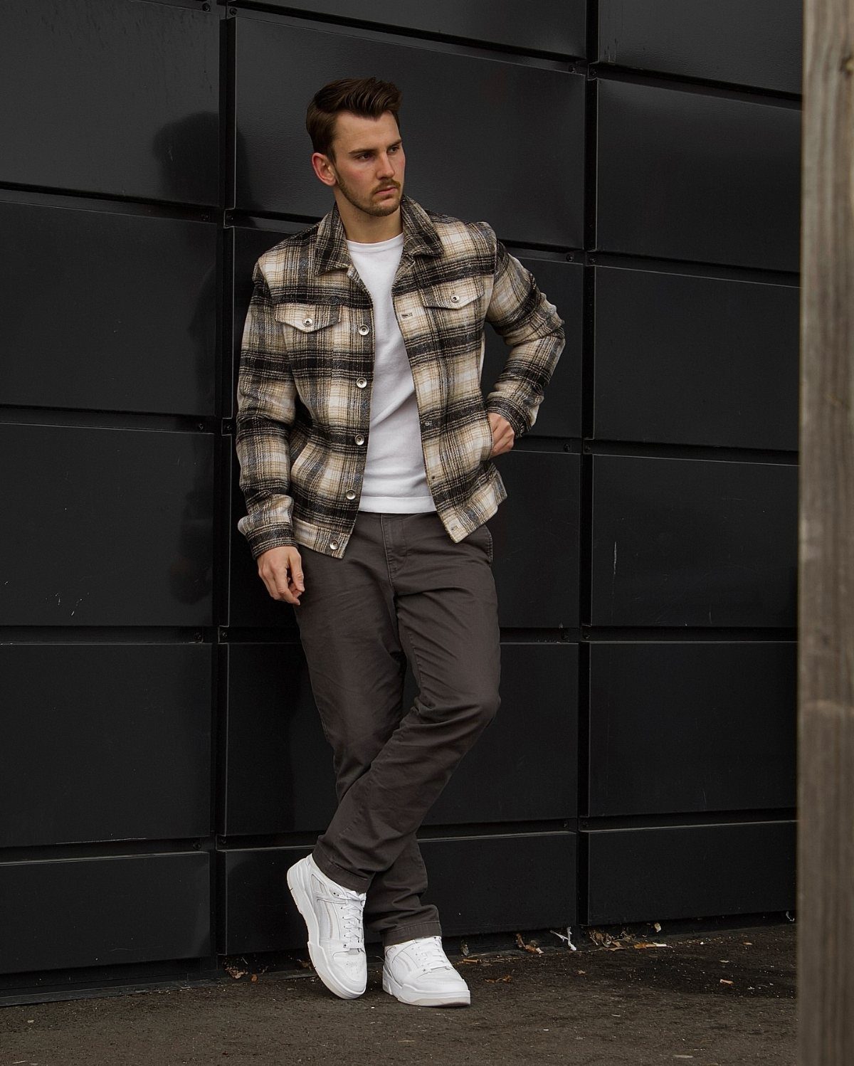 Man in plaid shirt and grey trousers wearing white lace-up sneakers
