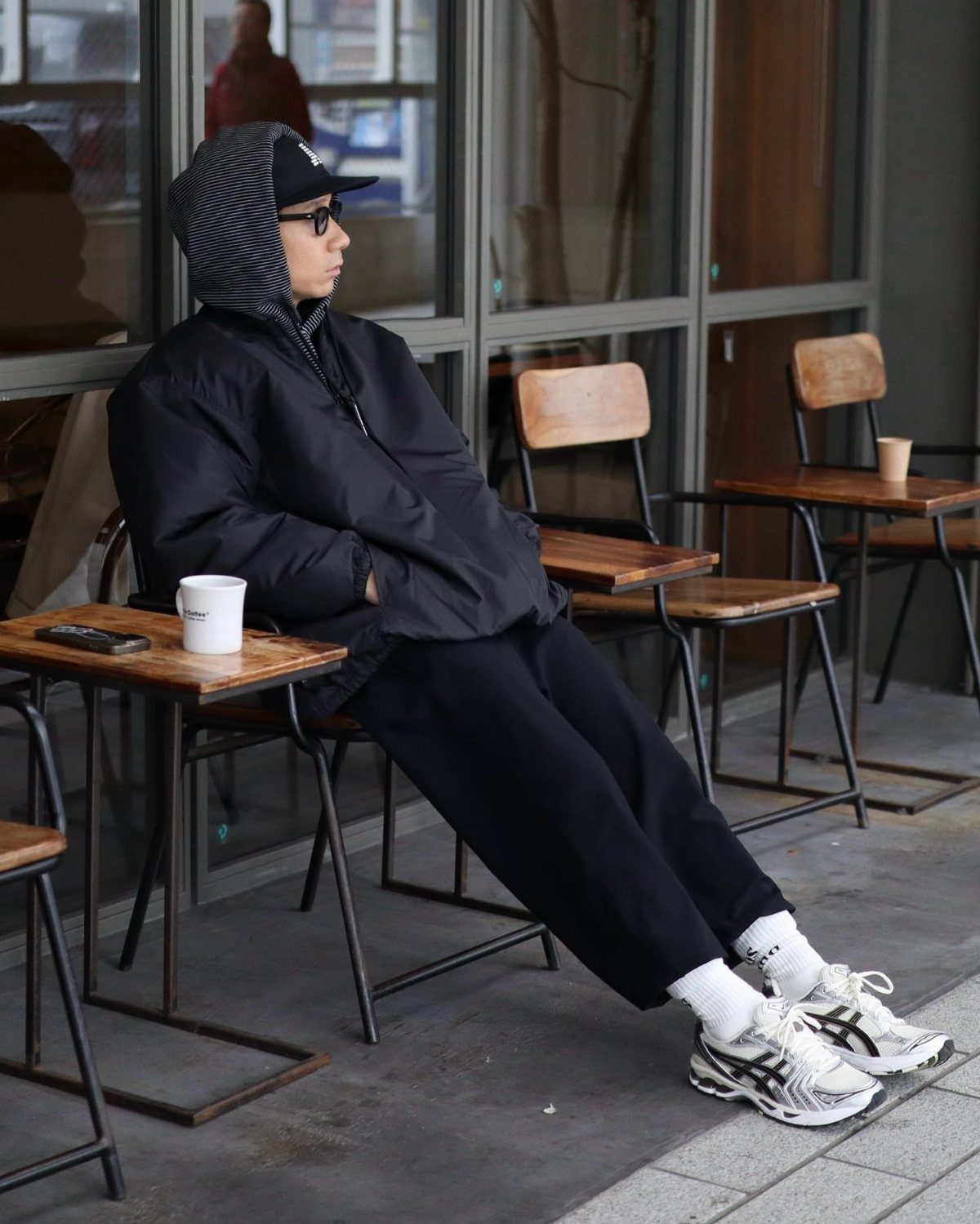 Man in black streetwear wearing chunky white dad shoes sitting at a cafe.
