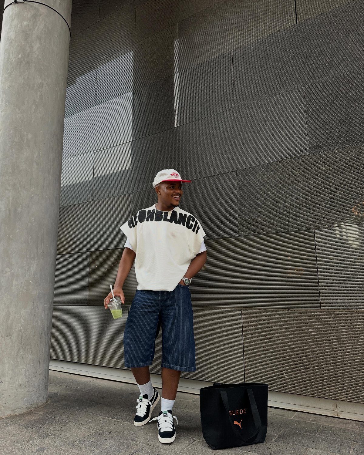 Man in white graphic tee and denim shorts wearing black and white sneakers.