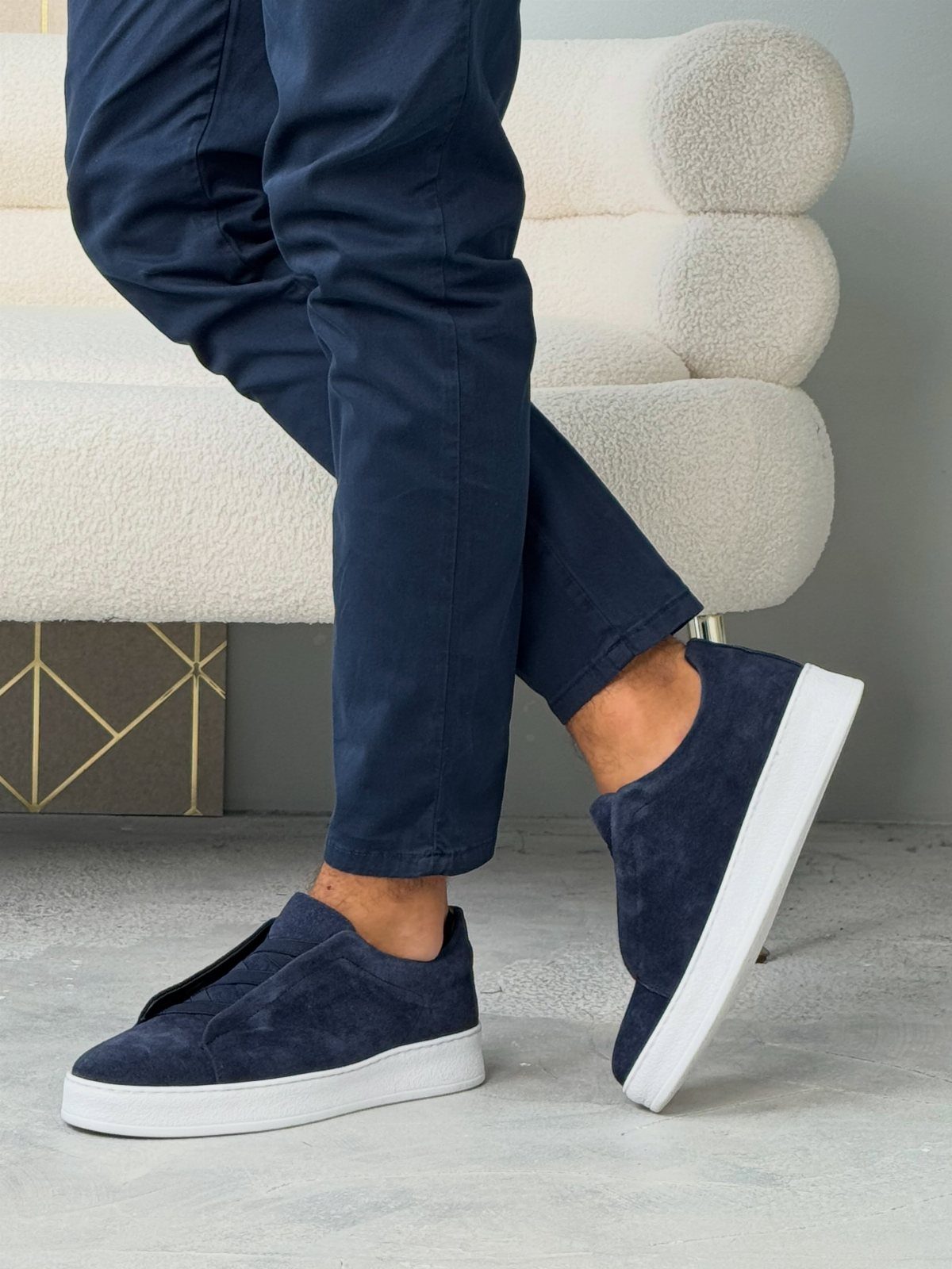 Navy blue suede slip-on sneakers with white soles paired with navy trousers.