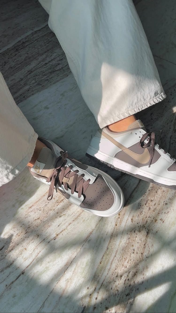 Neutral tone sneakers in beige and brown paired with off-white trousers on marble.