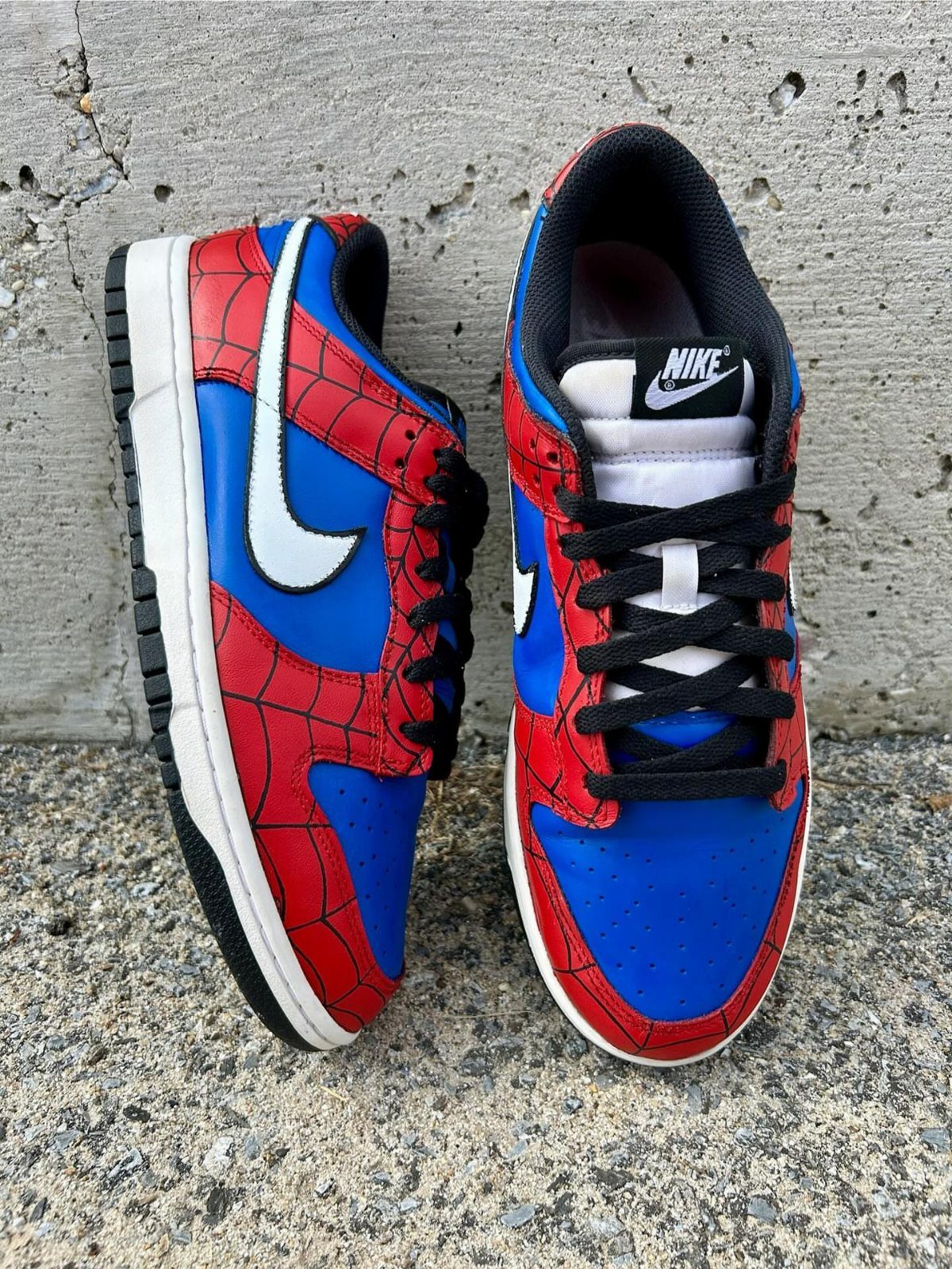 Customized Nike sneakers with red spiderweb patterns and blue accents on concrete.