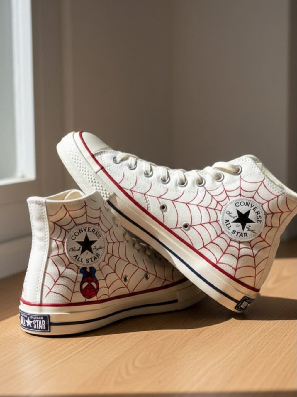 White high-top Converse sneakers with red spiderweb designs and a Spiderman graphic.