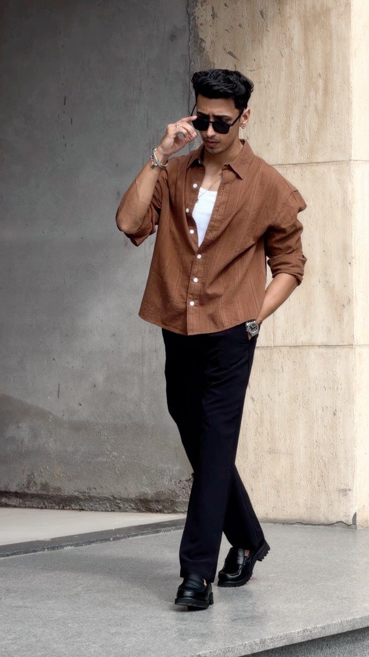 Man in brown shirt and black trousers wearing black leather loafers outdoors.