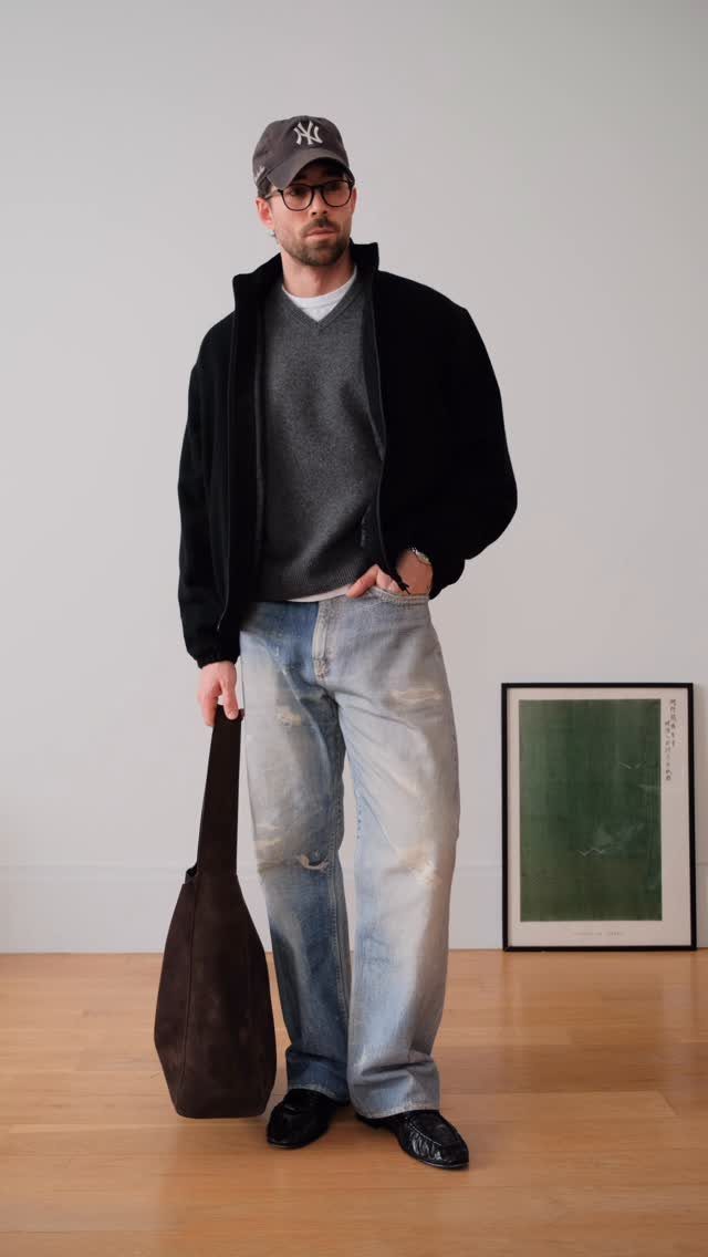 Man wearing light-wash blue jeans and black leather loafers with a black jacket.
