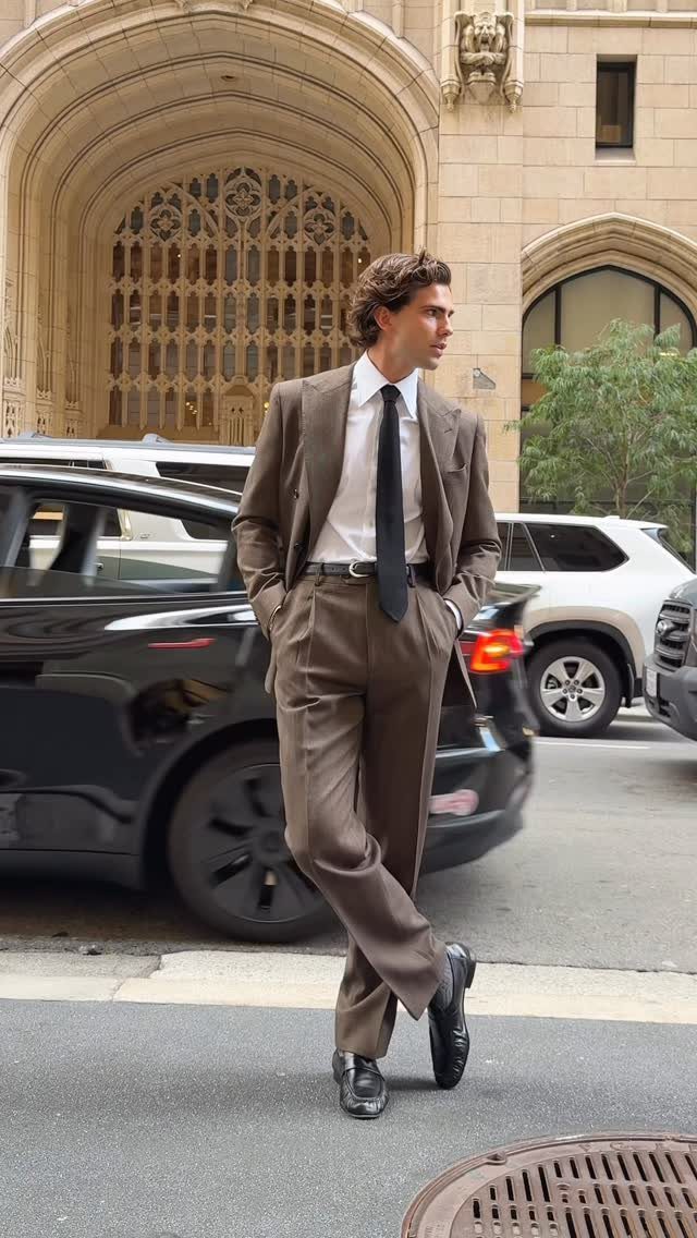 Man in a brown tailored suit and black loafers posing on a city street