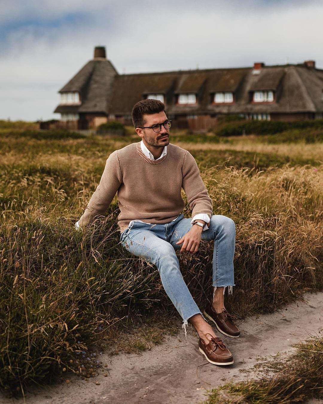 Man wearing tan sweater and light blue jeans with brown leather boat shoes.