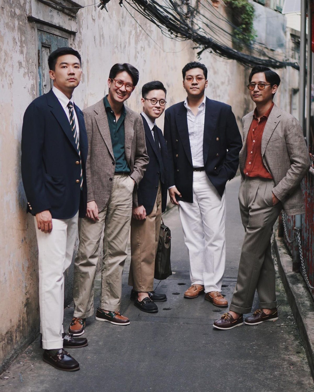 Five men in blazers and trousers wearing brown boat shoes in an alleyway