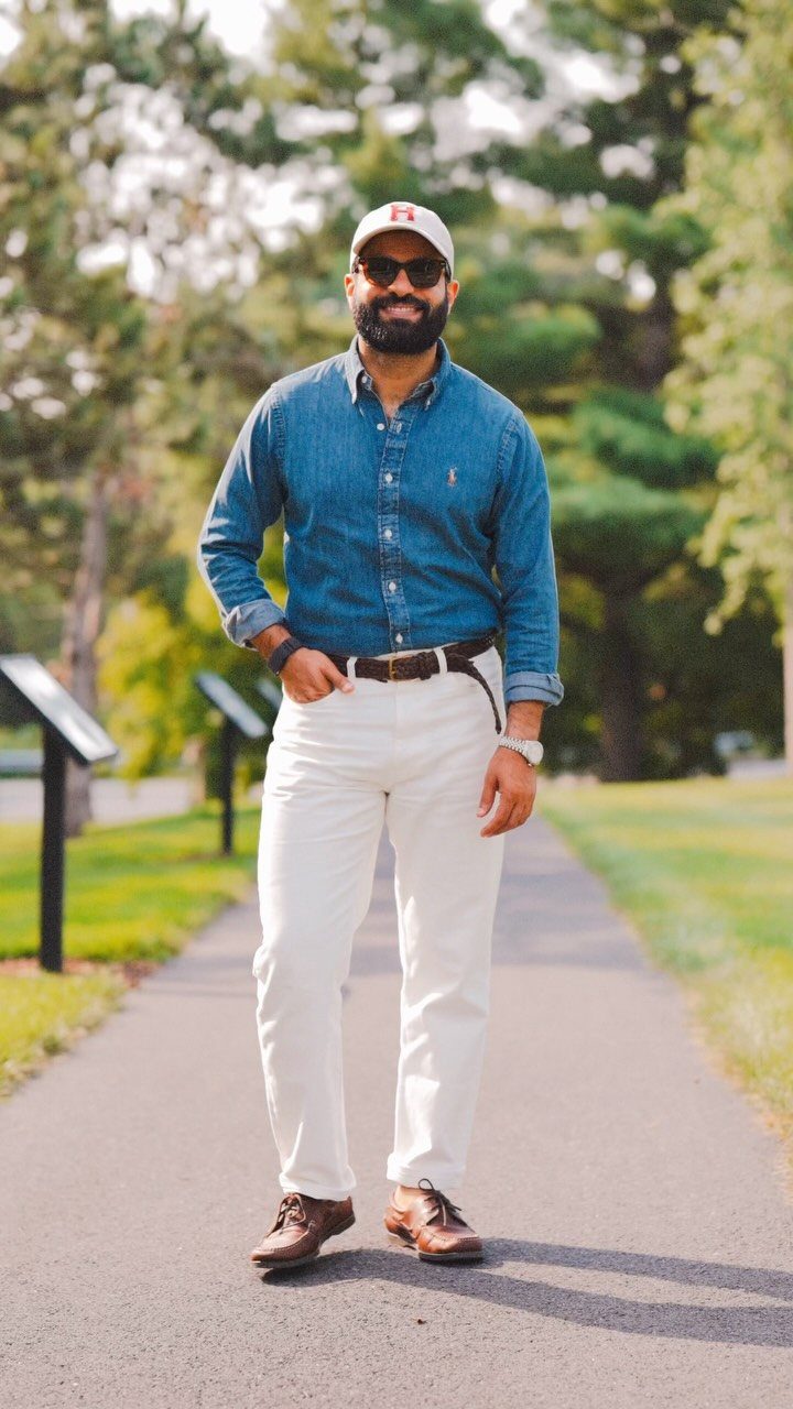 Man wearing a denim shirt, white pants, and brown leather boat shoes outdoors.