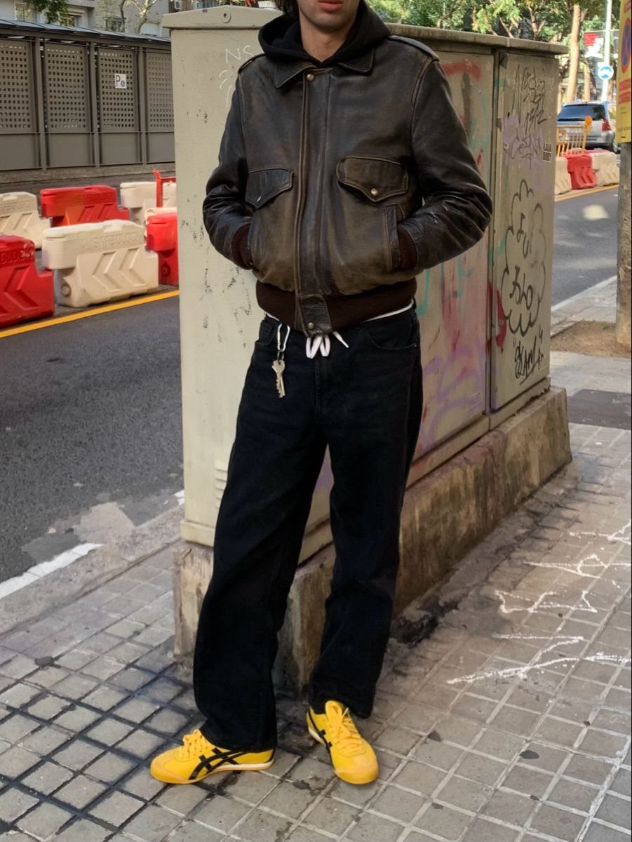 Person wearing a brown leather jacket, black trousers, and yellow Onitsuka Tiger sneakers.