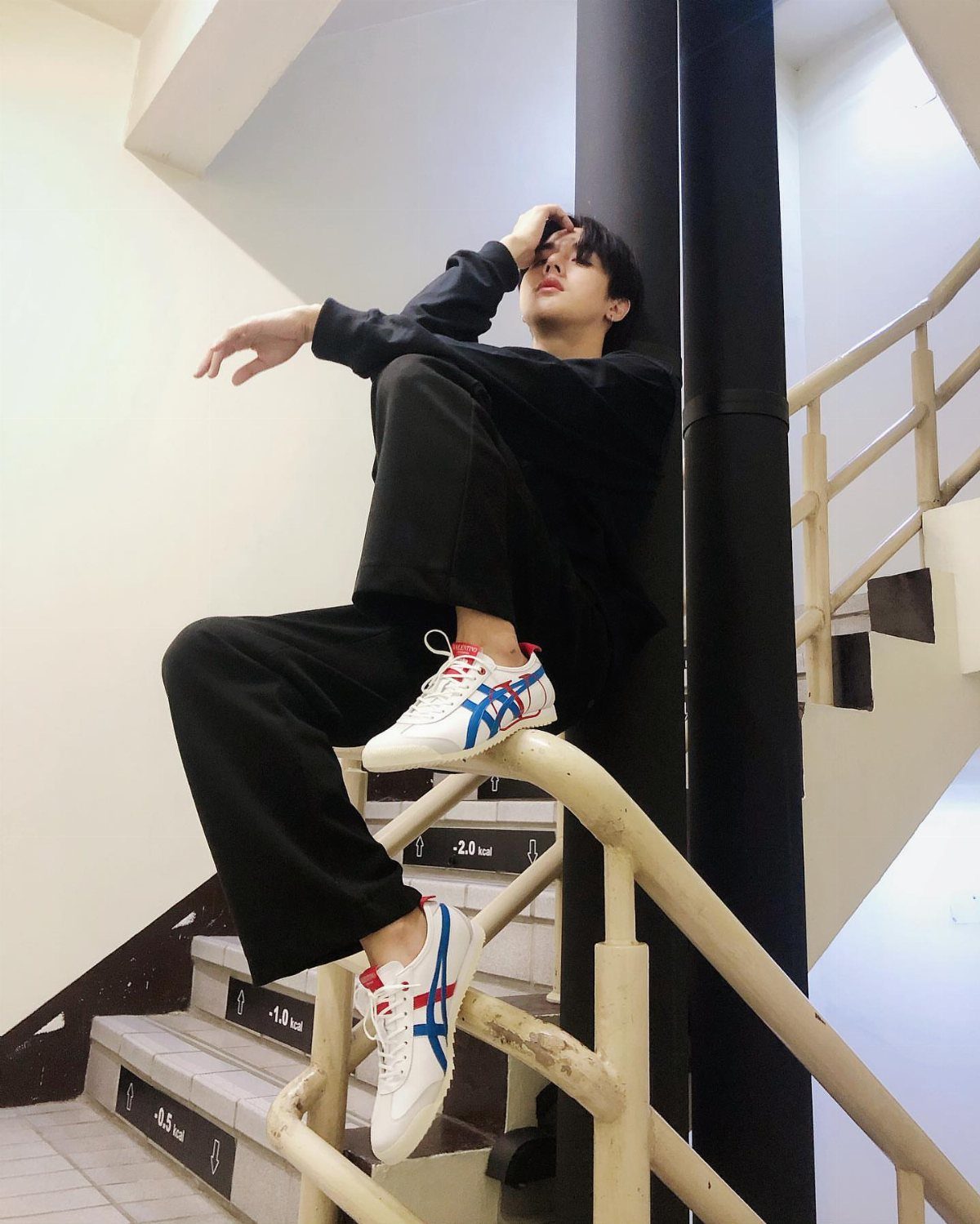 Person in oversized black top and wide-leg trousers wearing white Onitsuka Tiger sneakers.