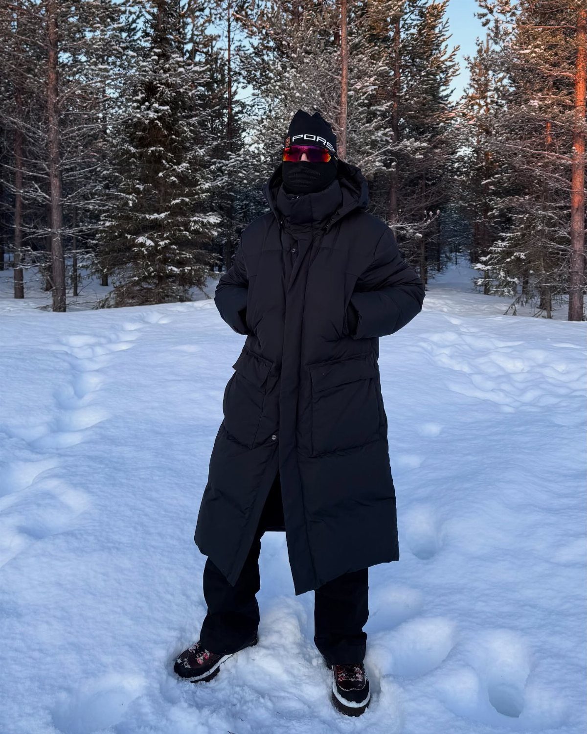 Person in black puffer coat, snow pants, and boots standing in snowy forest