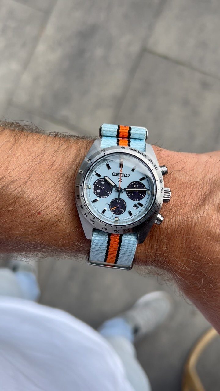Silver Seiko chronograph watch with light blue face and striped fabric strap on wrist