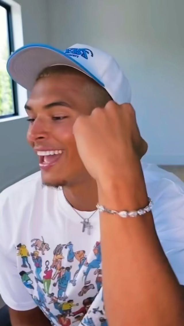 Smiling man wearing a white cap, silver chain, and beaded bracelet accessories.