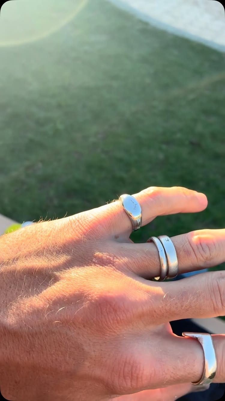 Man's hand wearing multiple silver metal rings against a blurred green grass background.