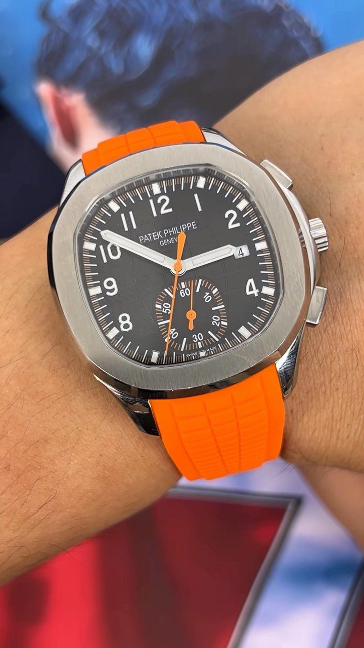 Silver Patek Philippe watch with a bright orange rubber strap on a wrist