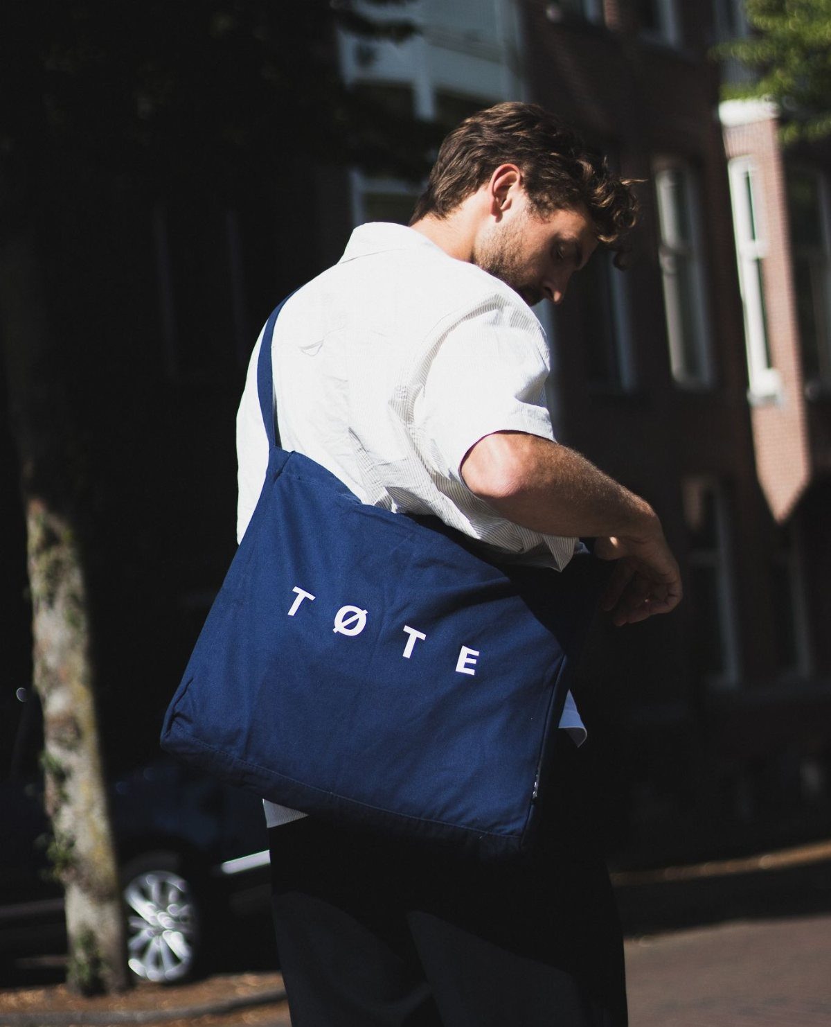 Man in white shirt carrying a navy blue canvas tote bag on a street