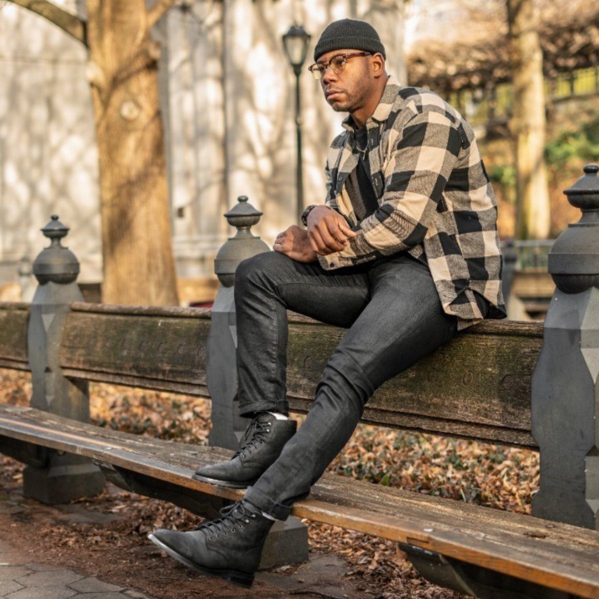 Man in plaid shirt and black jeans wearing black boots on park bench