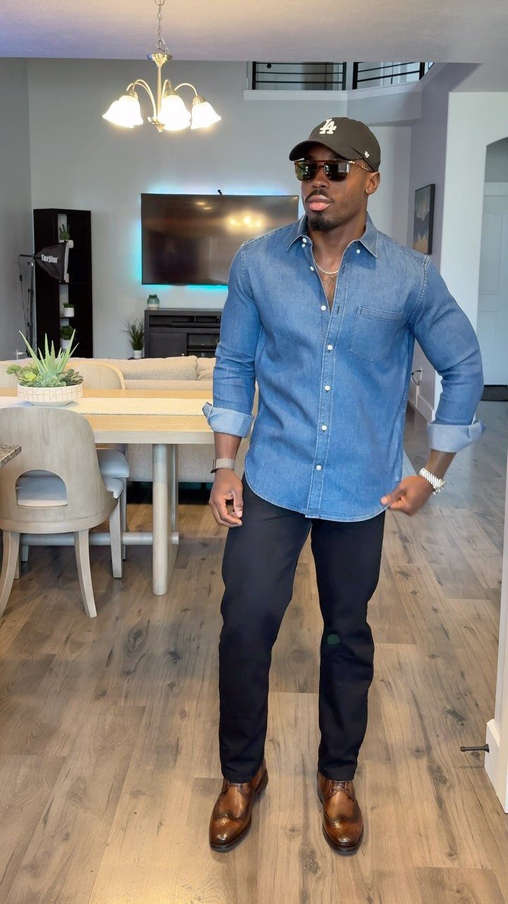 Man wearing a blue denim shirt, black pants, and brown leather boots.