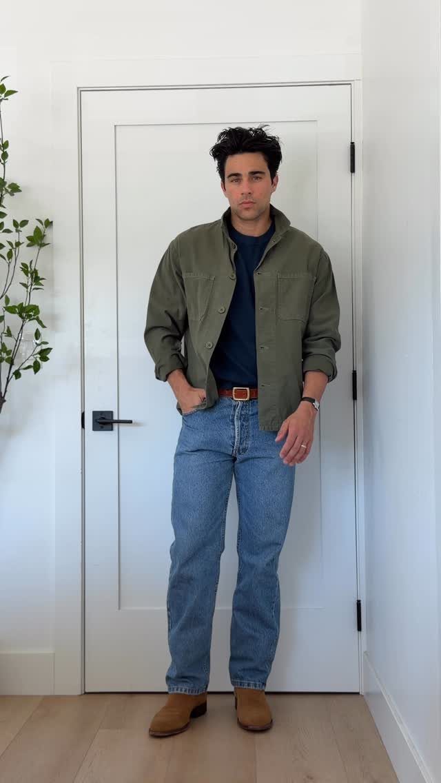 Man wearing olive overshirt, navy t-shirt, light blue jeans, and brown suede boots.