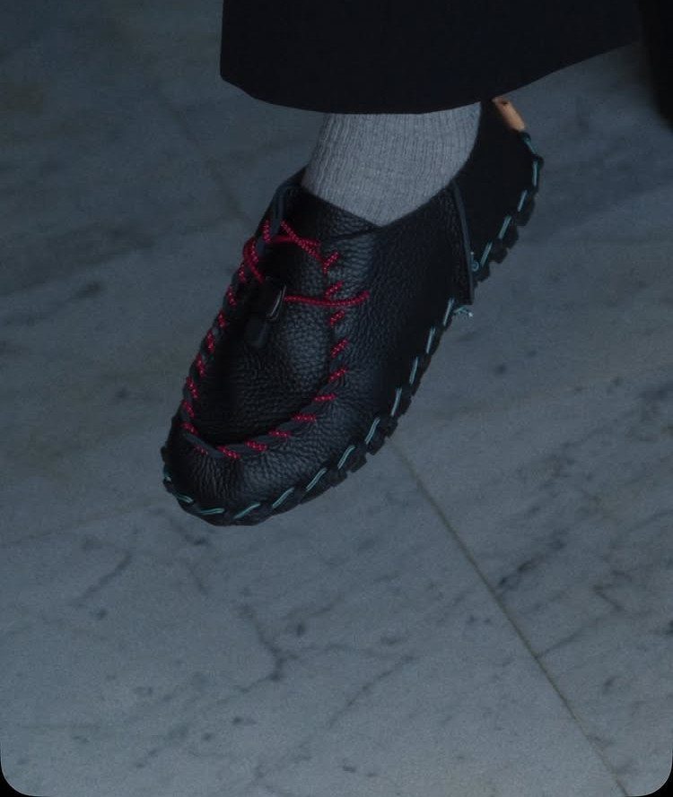 Black leather loafer with red and blue contrast stitching on a stone floor