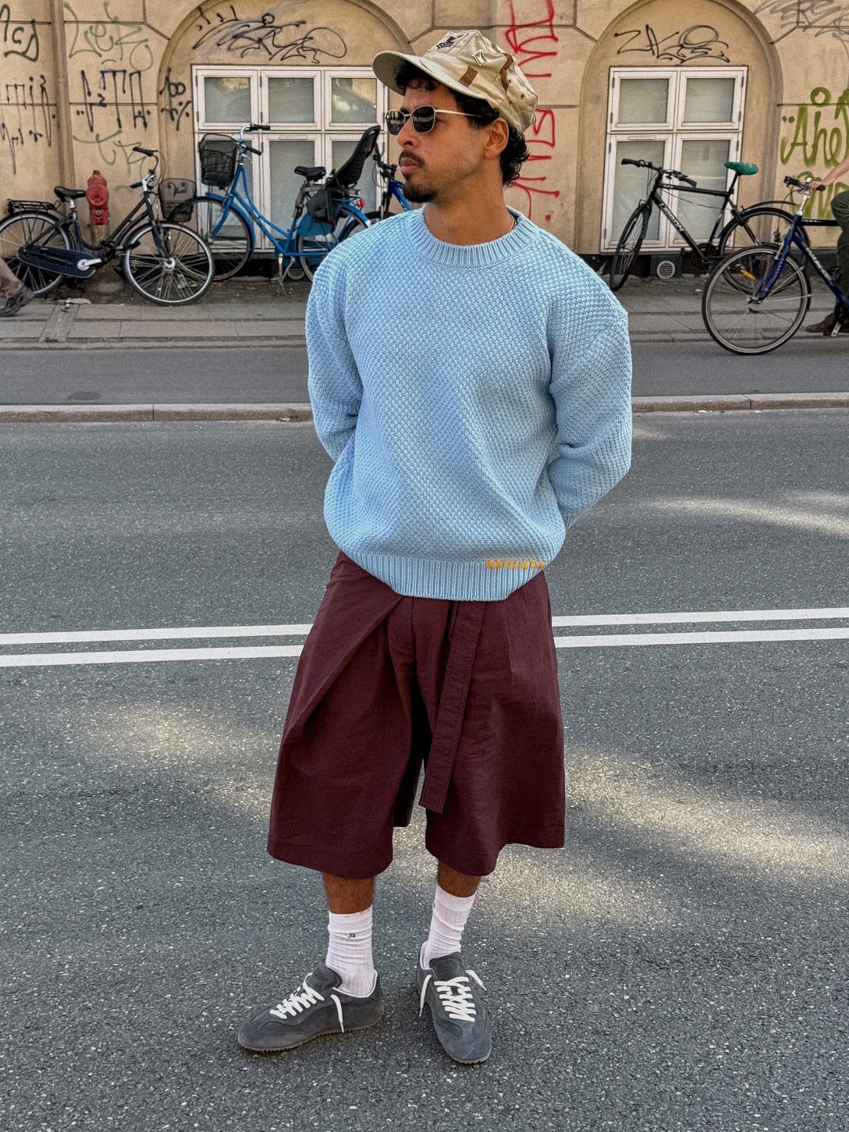 Man in blue sweater and maroon shorts wearing grey suede sneakers on street