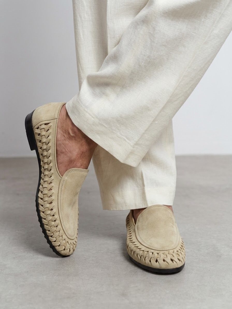 Beige woven leather loafers worn with wide-leg off-white linen trousers on grey floor.