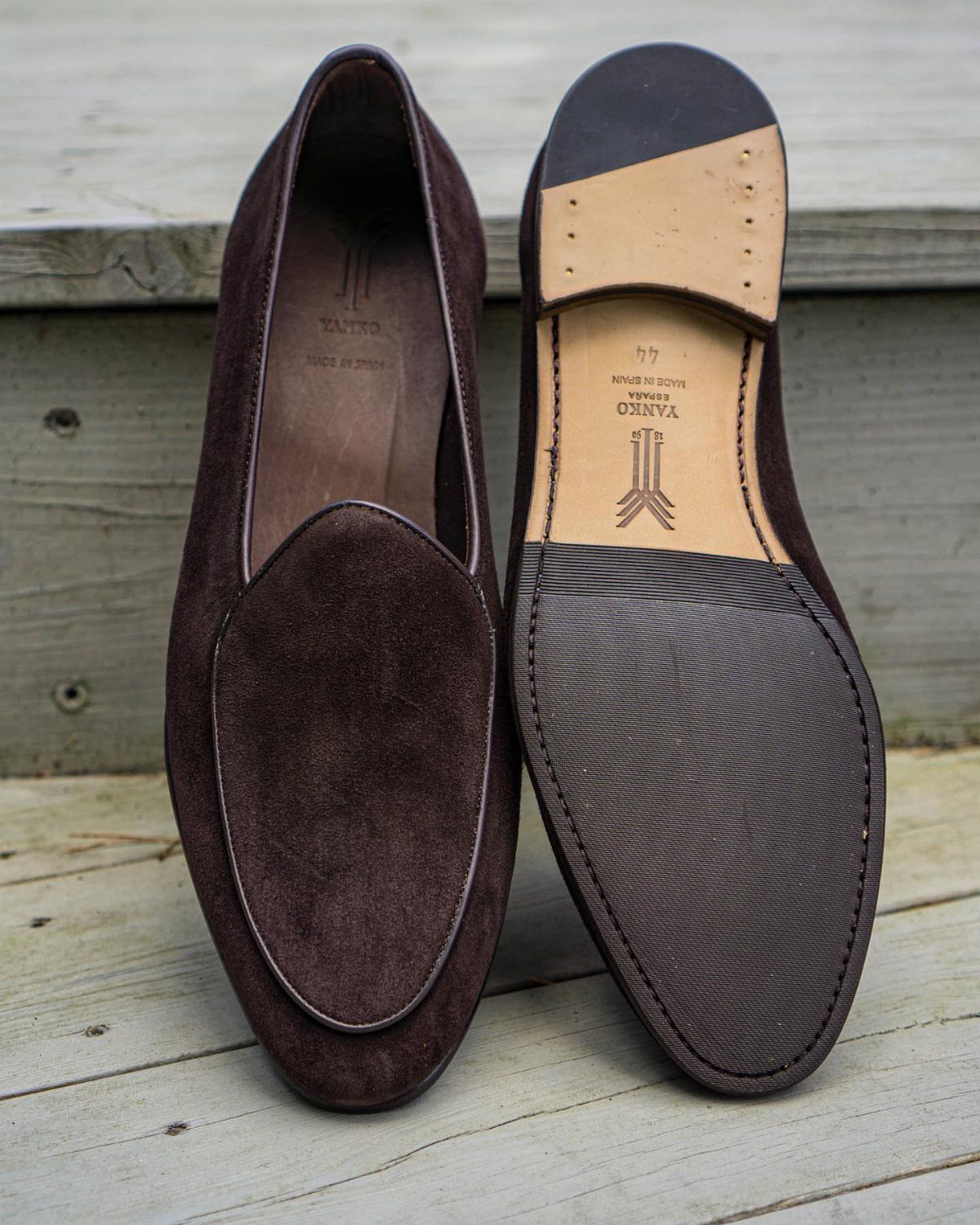 Dark brown suede Belgian-style loafers resting on a light wooden deck surface.