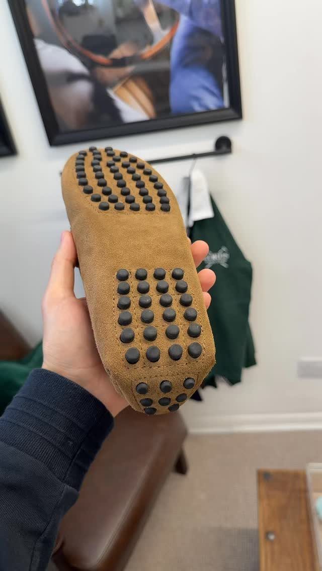 Tan suede driving shoe loafer showing the rubber nubbed sole held by a hand.