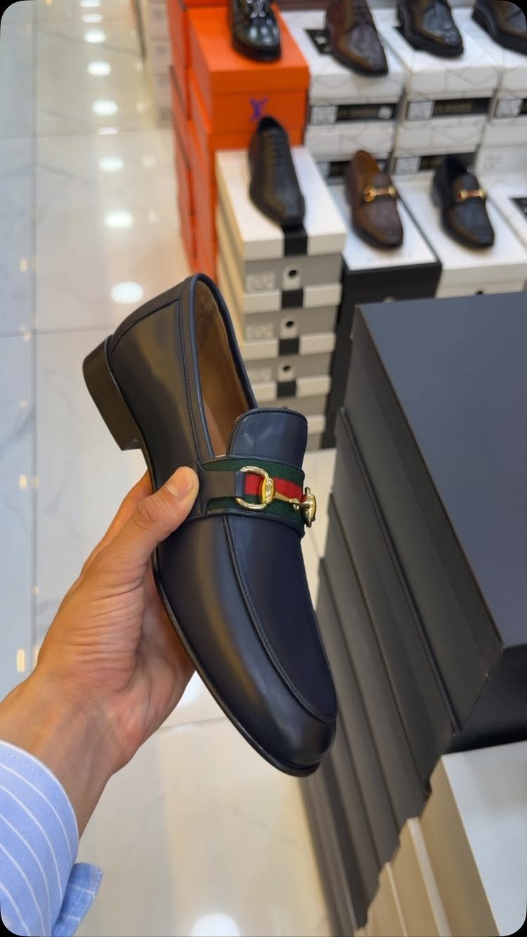 Dark blue leather horsebit loafer with gold metal bit and striped web detail.