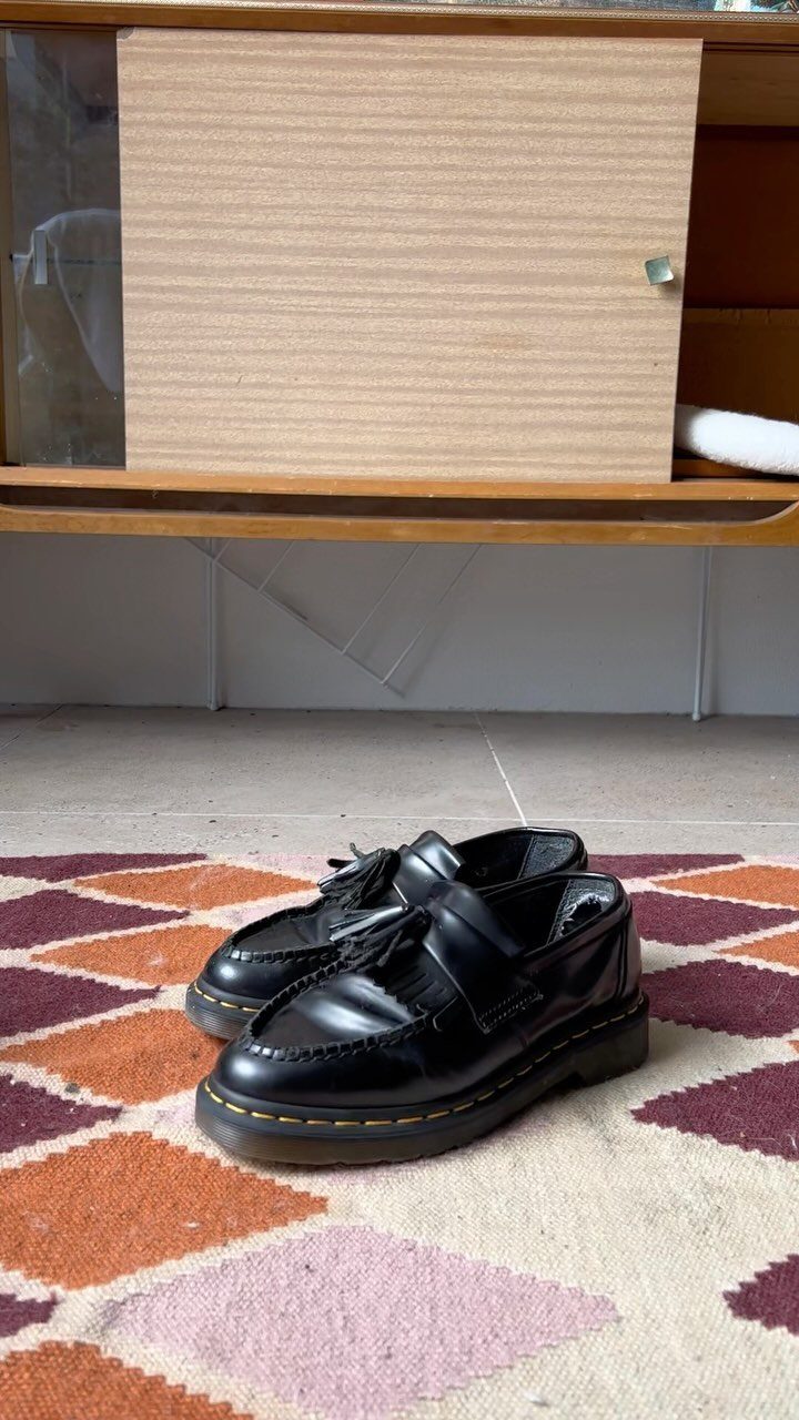 Black leather kiltie loafers with decorative fringes on a patterned rug.