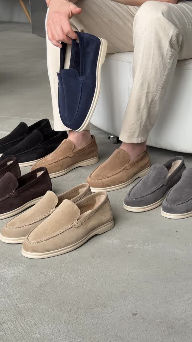Suede slip-on loafers in multiple colors arranged on a grey concrete floor.