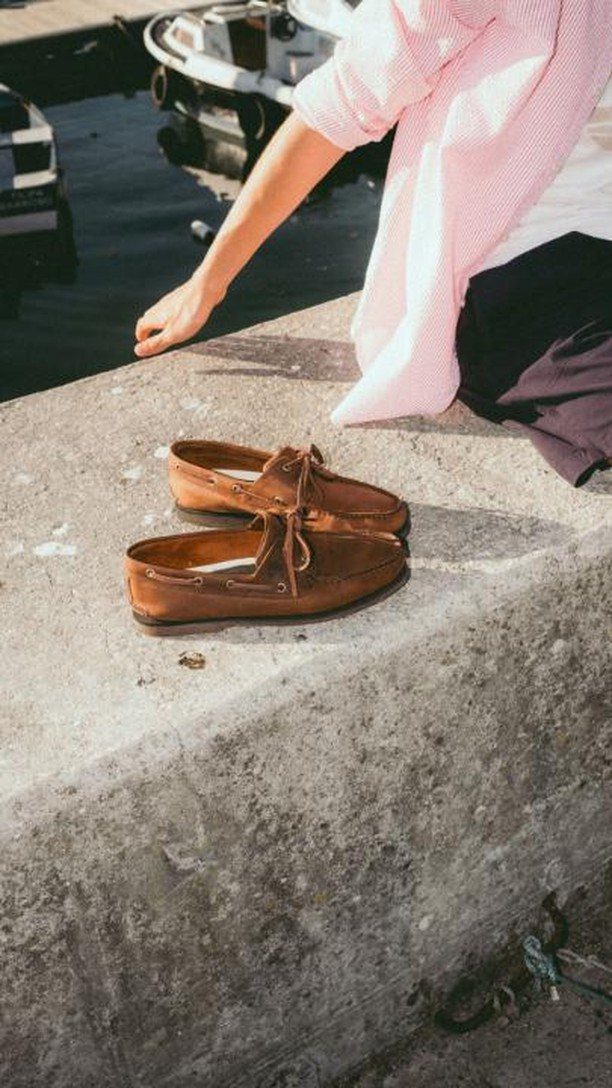 Brown leather boat shoes resting on a concrete ledge by the water.