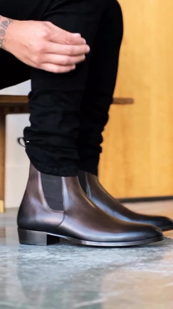 Dark brown leather Chelsea boots with elastic side panels worn with black trousers.