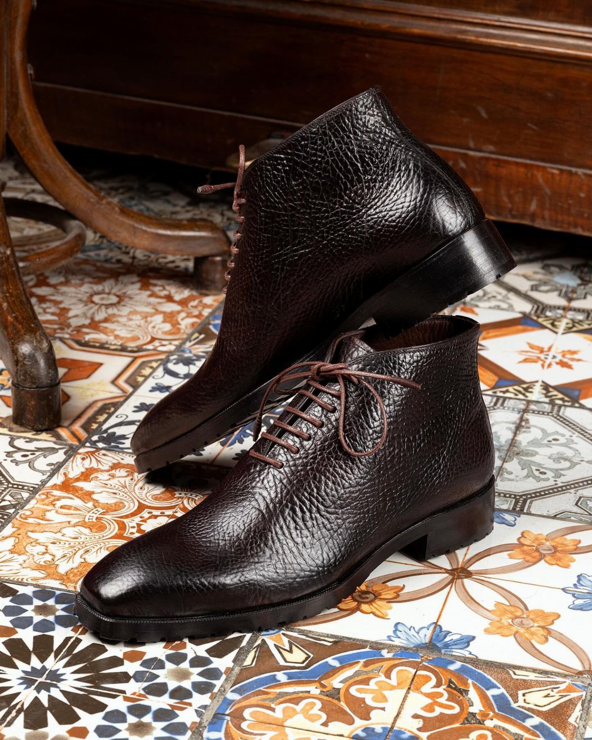 Dark brown textured leather dress boots with laces on patterned tile floor