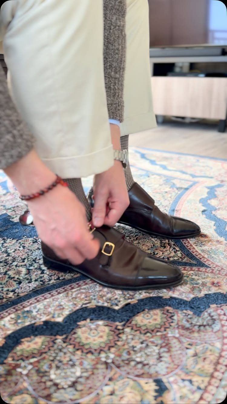Dark brown leather monk strap shoes with gold buckles on a patterned rug
