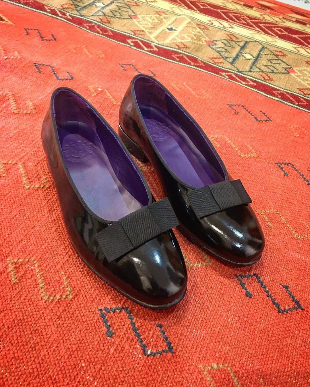 Black patent leather opera pumps with bows on a red patterned rug