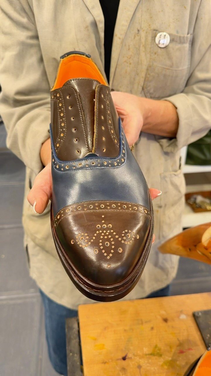 Two-toned navy and brown leather brogue shoe with decorative perforations held by hands.