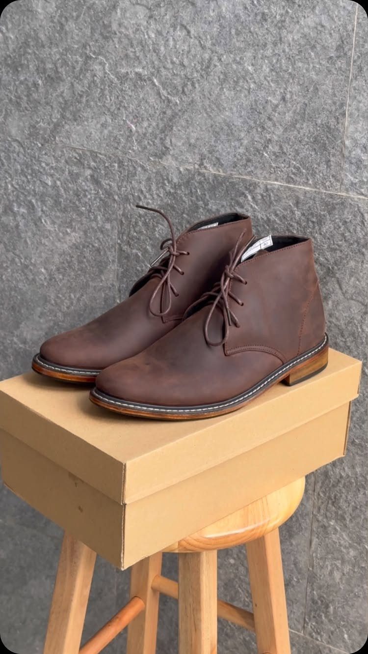 Brown leather chukka boots with laces sitting on a cardboard box and stool.