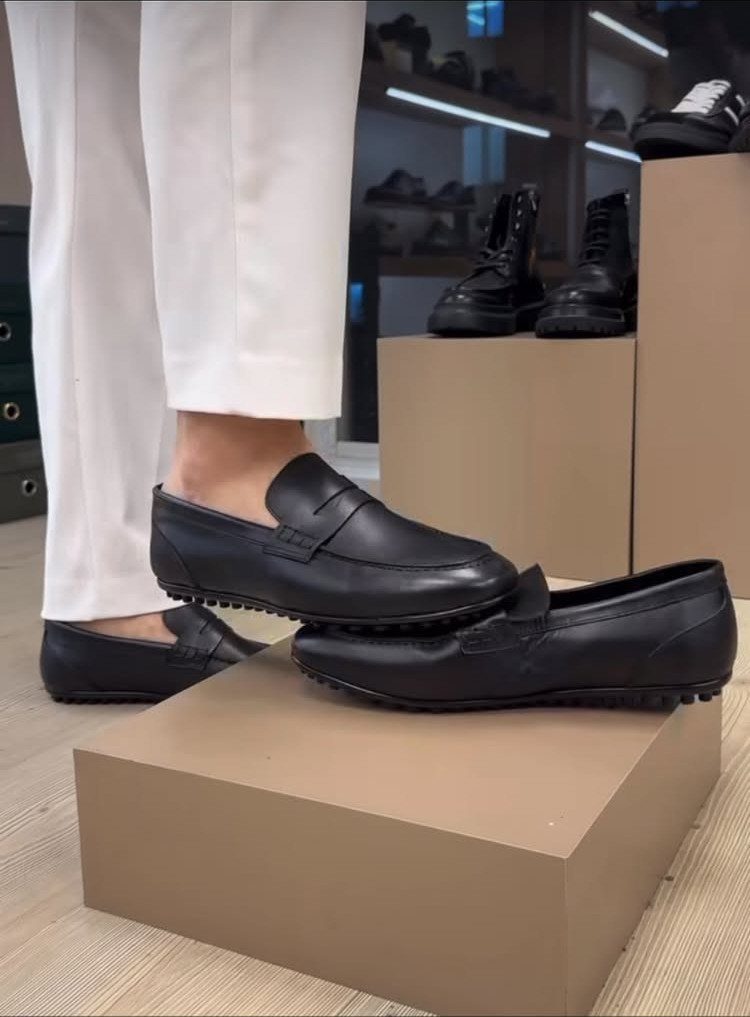 Black leather driving shoes with pebbled soles worn with white trousers.