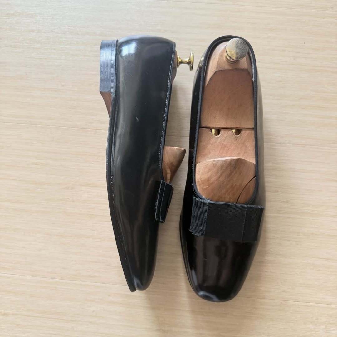 Black patent leather opera pumps with grosgrain bows on a wooden surface